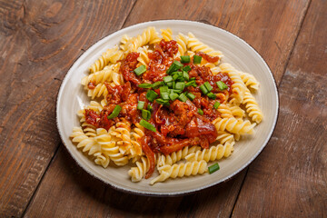 Beige plate with bolognese pasta on a wooden table sprinkled with green onions.