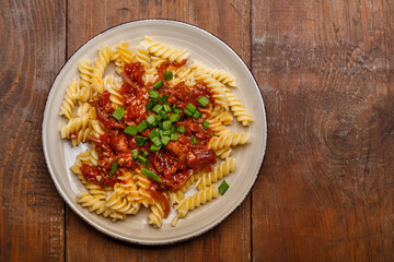 Plate with bolognese pasta on a wooden table sprinkled with green onions.