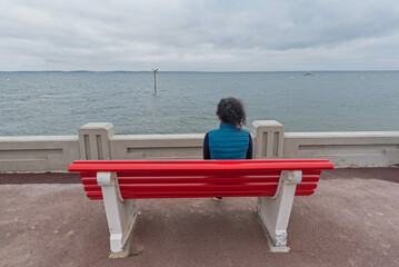 Woman looking at the sea sitting on a red bench