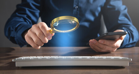 Man using magnifying glass over computer keyboard. Concept of searching internet