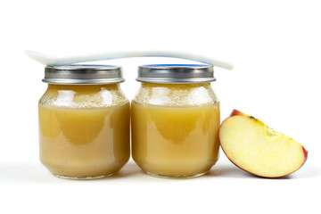Two glass jars with baby apple puree with a spoon and an apple slice on a white isolated background. The first fruit lure of the baby. Baby food.