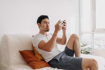 Funny asian man seriously focus on his mobile game in his relax day.