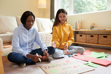 Teenage girl helping friend to make placard for protest against climate change