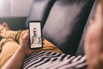 Woman lying on a sofa and talking with a doctor online using mobile phone. Telemedicine concept. - obrazy, fototapety, plakaty