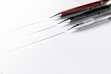 Three mechanical pencils with lines on paper of different sizes on the white background.