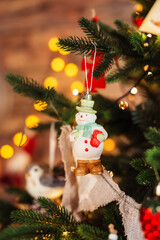 A toy snowman on a branch of a Christmas tree, on the background of a garland.