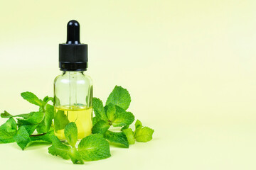 Essential oil of fragrant mint (peppermint) in a glass bottle with a pipette on a yellow background. Space for text. Aromatherapy (against fatigue, headache, relaxation), spa, skin care.
