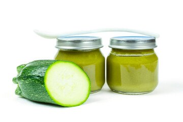 Two glass jars with lids of baby squash puree (zucchini) and a spoon on a white insulated background. Baby food. The first lure of the baby.