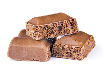 Pieces of porous milk chocolate lying on top of each other on a white isolated background close-up.