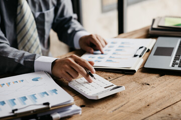 A businessman is using a white calculator to calculate financial numbers, he is sitting in his private office, the businessman examines the financial data from the corporate finance chart.