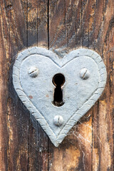 Historical door lock in the shape of a heart on a medieval wooden door.