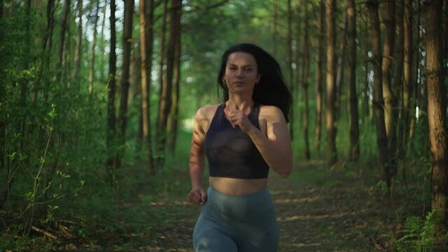 Athletic beautiful Caucasian girl on a morning jog. Woman running through the woods in beautiful nature, active sports in nature.