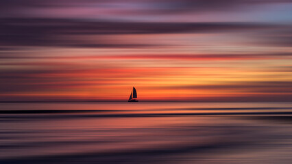 Fototapeta na wymiar Tropical beach sunset with yacht. Motion blur to clouds and sea. A sail boat at sea, with colorful sky backdrop and reflections and motion blur making a beautiful, dreamlike seascape