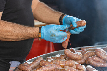 Unrecognizable cook putting sausages on the grill, concept gastronomy, selective approach to the right hand.