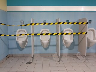 Closed men's room with white  public toilets porcelain urinals with black and yellow striped tapes....