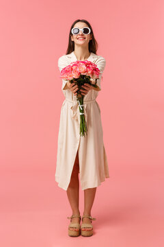 Full-length Vertical Portrait Attractive Sassy And Stylish Brunette Woman Giving Flowers To Her Girlfriend, Extending Hands Towards Camera Holding Nice Bouquet Roses, Standing Pink Background