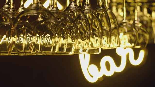 Bar and alcohol concept . Different types of transparent glasses on the hanger above a bar counter at a fancy restaurant . Empty wine glasses hang upside down in a row at a rack in hotel . Dolly shot