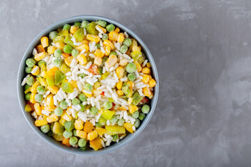 Bowl with mixed frozen vegetables with rice on a gray background. Frozen vegetables retaining all nutrients: green peas, corn, bell pepper. Healthy food concept. Top view. Copy space