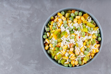 Bowl with mixed frozen vegetables with rice on a gray background. Frozen vegetables retaining all nutrients: green peas, corn, bell pepper. Healthy food concept. Top view. Copy space