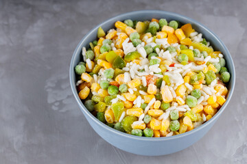 Bowl with mixed frozen vegetables with rice on a gray background. Frozen vegetables retaining all nutrients: green peas, corn, bell pepper. Healthy food concept. Top view. Copy space