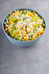 Bowl with mixed frozen vegetables with rice on a gray background. Frozen vegetables retaining all nutrients: green peas, corn, bell pepper. Healthy food concept. Top view. Copy space