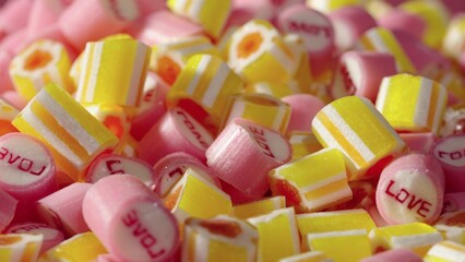 Colored striped caramel candies with inscription Love, rotating shot. Mix of pink and yellow lollipops close up. Sweet sugar dessert. Candy Shop. Festive background for holiday or children's birthday.