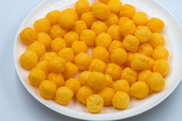 Selective focused cheese puff balls.  Pile of cheese balls isolated on white background. Plate full of cheese puff balls isolated