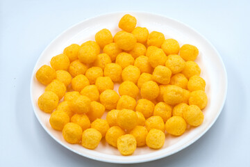 Selective focused cheese puff balls.  Pile of cheese balls isolated on white background. Plate full of cheese puff balls isolated