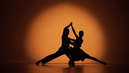 Een paar dansers naderen elkaar en beginnen Argentijnse tango te dansen. Elementen van latin ballroomdans in studio met oranje bruine achtergrond. Donkere silhouetten. Klaar voor slow motion, 4K met 59,94 fps.
