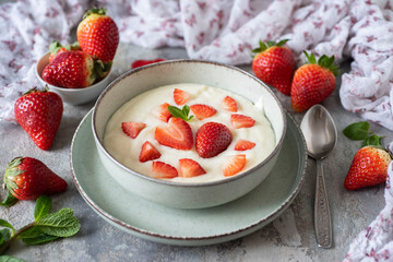 Delicious breakfast for children: sweet milk semolina porridge with strawberries on a beautiful plate, strawberries on a gray background. Semolina porridge with milk for lunch.