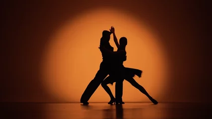 Fototapete Tanzschule Couple of dancers approach each other and begin to dance Argentine tango. Elements of latin ballroom dance in studio with orange brown background. Dark silhouettes. Slow motion ready, 4K at 59.94fps.  © kinomaster