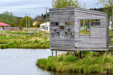 An elevated wooden duck blind beside a pond in a park. Many rectangular holes to look through....