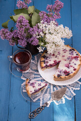 Homemade berry pie with a cup of tea on the table with a bouquet of lilacs.