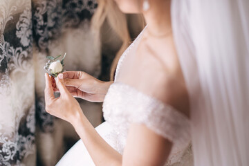 The bride holds a boutonniere with a white rose in her hands, waiting for the groom.