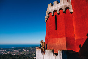 A young beautiful couple stands on top of the Pena National Palace in Portugal against the backdrop...