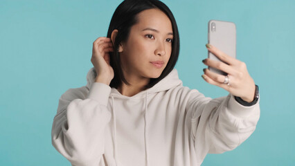 Fototapeta premium Asian girl looking confident holding smartphone making selfie over colorful background. Millennial content maker