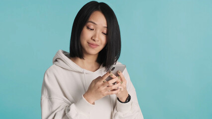 Attractive Asian woman wearing white hoodie chatting with boyfriends using smartphone on blue background