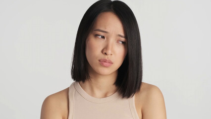 Close up sad Asian woman looking depressed standing over white background. Displeased face