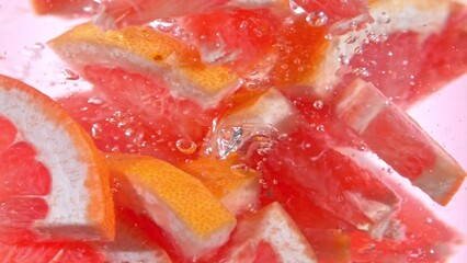 Super Slow Motion Shot of Fresh Pink Grapefruit Slices Falling into Water Vortex at 1000 fps.