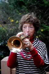 Female senior trumpet player blowing her horn outside.
