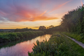 The sun sets behind a hill of trees making the gorgeous orange sky look like it is on fire as the...