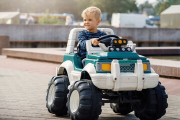 Close up portrait of young happy kid driving electric toy car outdoors.