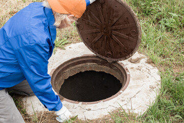 A working plumber opens a sewer hatch. Maintenance of septic tanks and water wells