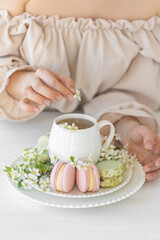 Traditional delicious French dessert - sweet homemade macarons on a vintage plate. Colourful tasty macaroons served on a white china with herbal tea. Decorated with fragile cherry tree flowers.