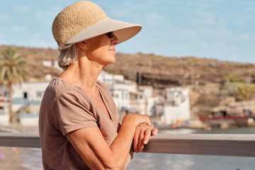 Mujer jubilada con sombrero disfrutando de la vista del mar al atardecer.