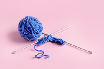 Blue knitted wool on a pink background with knitting needles for knitting warm clothes and hobbies needlework