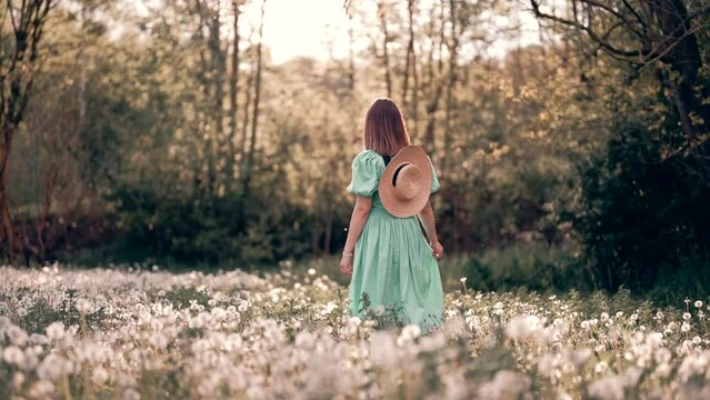 Retro styled woman walking on fluffy dandelions field, amazing fantasy steadicam footage. Romantic girl with hat on nature. Vintage aesthetic lifestyle, floral background.
