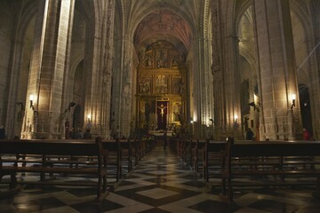 Fototapeta premium The faithful slowly gathering for Sunday mass under the gray stone Gothic arches of sparsely lit Iglesia de San Miguel church, Jerez de la Frontera, Spain