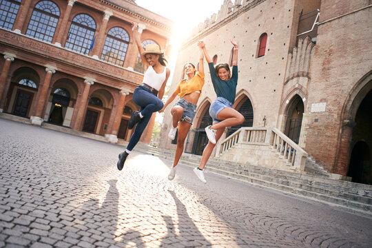 Happy women having fun together in Venice. Three young women jump holding hans, multiracial group laughing together. Lifestyle, freedom, celebration and friendship concepts