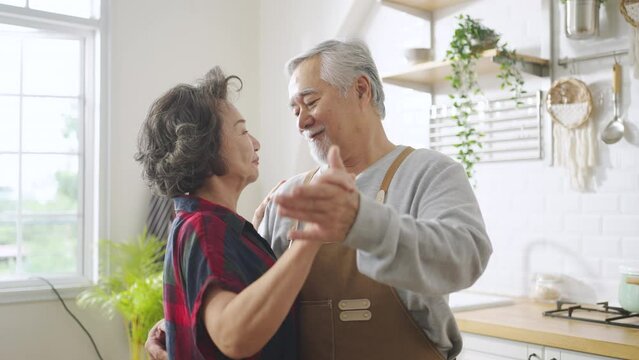 Asian mature senior couple is dancing and smiling in kitchen at home.